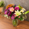 Fall Colors Designers Choice bouquet with lilies, chrysanthemums, carnations, and daisies in warm autumn tones, arranged in a clear glass vase.