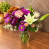 Fall Colors Designers Choice bouquet with lilies, chrysanthemums, carnations, and daisies in warm autumn tones, arranged in a clear glass vase.