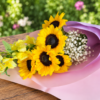 Cascading Sun bouquet featuring radiant sunflowers, lavender accents, and smaller yellow blooms, wrapped in pastel paper, handcrafted by allthepeoplesflowers.com for Cincinnati and Northern Kentucky delivery.