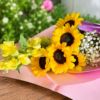 Cascading Sun bouquet featuring radiant sunflowers, lavender accents, and smaller yellow blooms, wrapped in pastel paper, handcrafted by allthepeoplesflowers.com for Cincinnati and Northern Kentucky delivery.