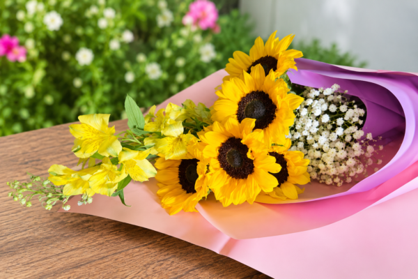 Cascading Sun bouquet featuring radiant sunflowers, lavender accents, and smaller yellow blooms, wrapped in pastel paper, handcrafted by allthepeoplesflowers.com for Cincinnati and Northern Kentucky delivery.