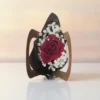 A single red rose wrapped in black and brown paper, surrounded by white baby’s breath, resting on a white surface with a softly blurred warm background.