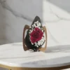 A single red rose wrapped in black and brown paper, surrounded by white baby’s breath, resting on a white surface with a softly blurred warm background.