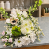 White and cream bouquet with blush pink flowers, a green layered bloom, a dark-centered cream flower, delicate white filler flowers, and trailing green foliage.