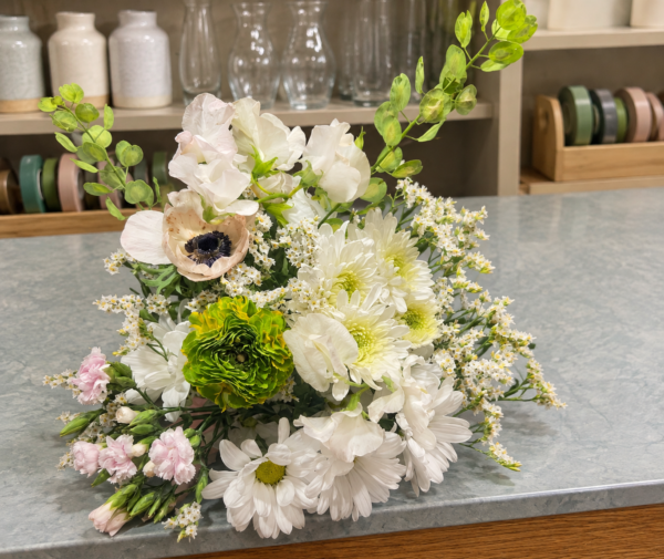 White and cream bouquet with blush pink flowers, a green layered bloom, a dark-centered cream flower, delicate white filler flowers, and trailing green foliage.