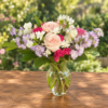 Exotic Floral Bouquet featuring blush pink roses, lavender stock, bright pink carnations, white accent blooms, and greenery arranged in a clear glass vase.