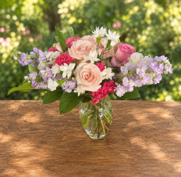 Exotic Floral Bouquet featuring blush pink roses, lavender stock, bright pink carnations, white accent blooms, and greenery arranged in a clear glass vase.